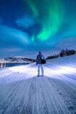 Man walking on a snowy road under northern lights
