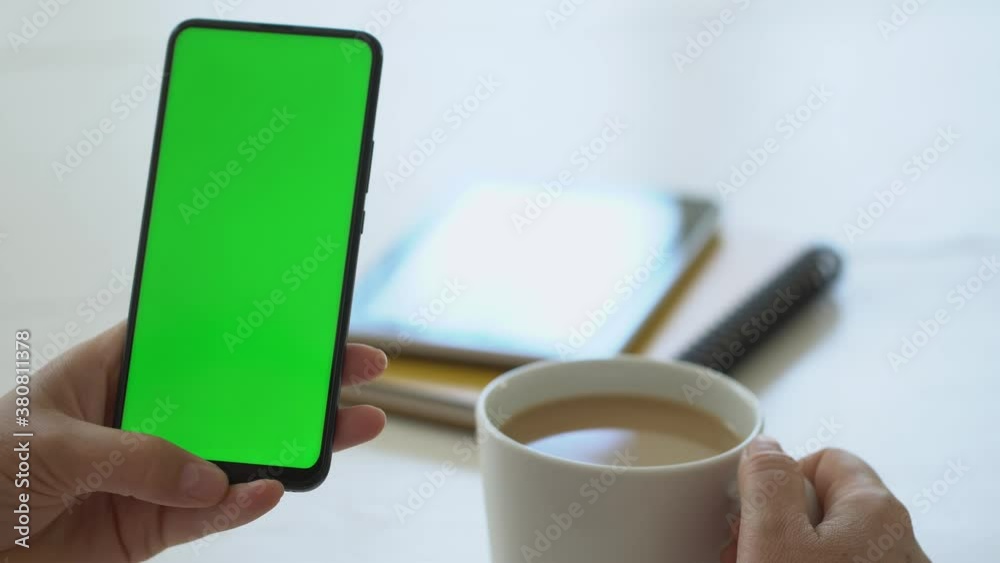Handheld Camera: business woman using smartphone viewing green screen on mobile phone browsing chroma key online watching enjoying drinking coffee reading social media close up hands Handheld Camera: business woman using smartphone viewing green screen on mobile phone browsing chroma key online watching enjoying drinking coffee reading social media close up hands