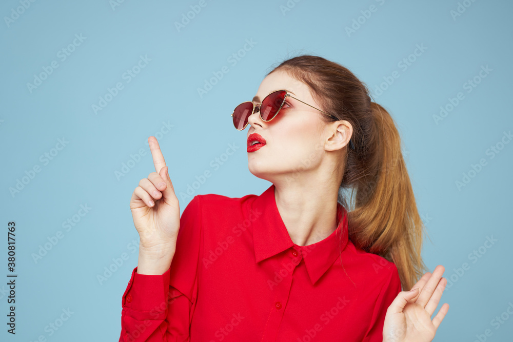 Beautiful woman in dark glasses red shirt bright makeup emotions attractive look blue background Beautiful woman in dark glasses red shirt bright makeup emotions attractive look blue background