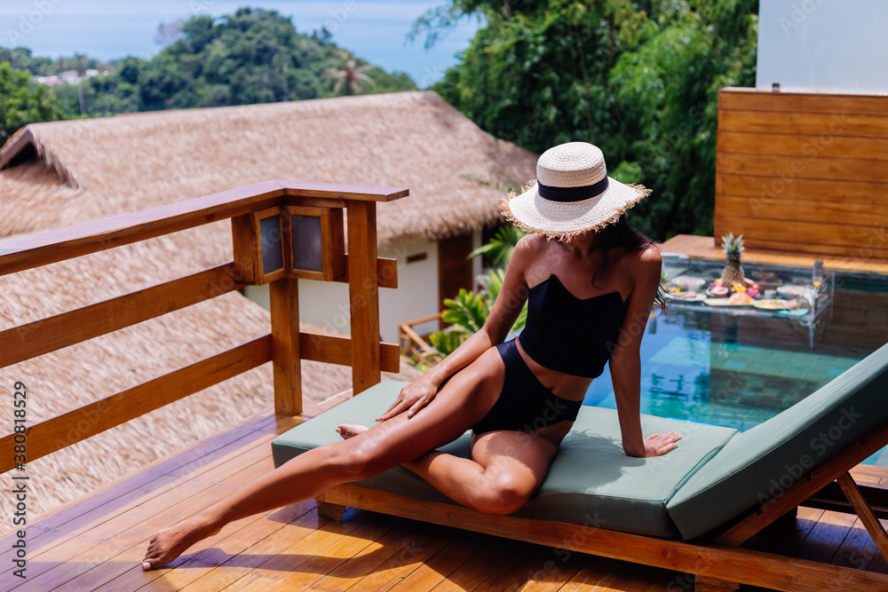 View of pretty tanned bronze perfect skin woman in black vintage old bikini lies on green sun bed at amazing villa at sunny day, resting, enjoying vacation. 