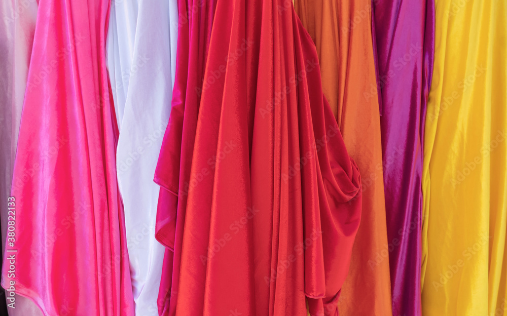 A selection of colorful clothing as a background, a variety of colorful rainbow fabrics, multi-colored curtain fabric backgrounds, a colorful blank sheet silk texture.