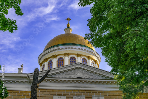 Golden dome of the Transfiguration Cathedral of the Saviour against the blue sky in Dnipro (Ukraine). Temple roof with cross among summer green trees, bottom view. Background with copy space