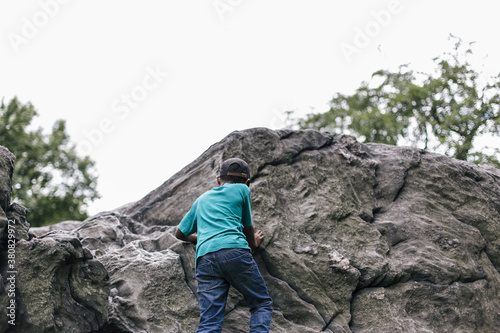 Behind shot of a young african american boy climbing up a rock photo