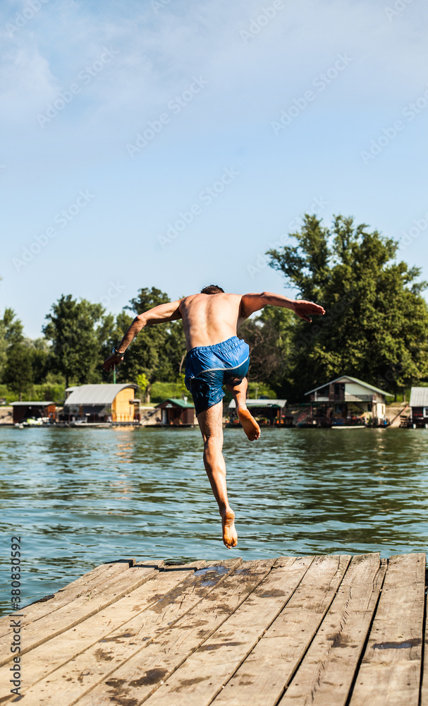 Young man jumping into river from wooden dock. Young man jumping into river from wooden dock.