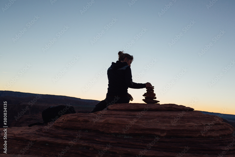 Woman stacking stones on the rock at sunset Woman stacking stones on the rock at sunset