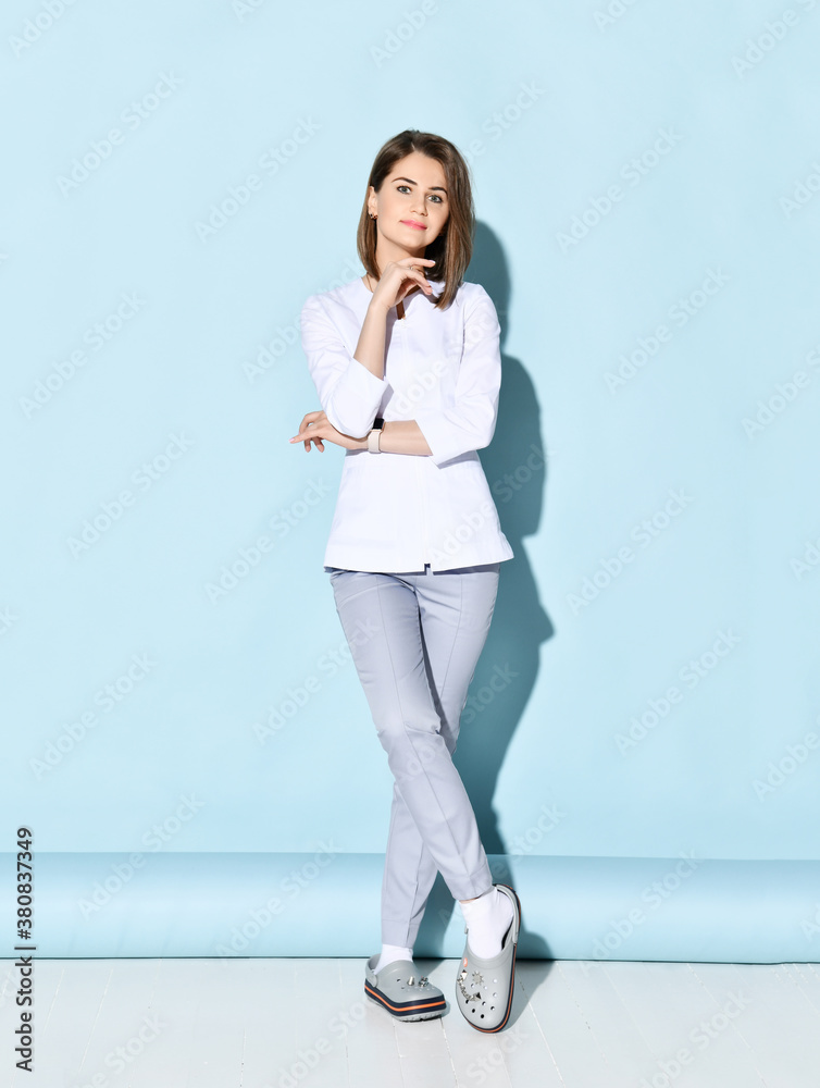 Young smiling woman dentist or doctor orthodontist in traditional white medical uniform stands and looks at camera Young smiling woman dentist or doctor orthodontist in traditional white medical uniform stands and looks at camera