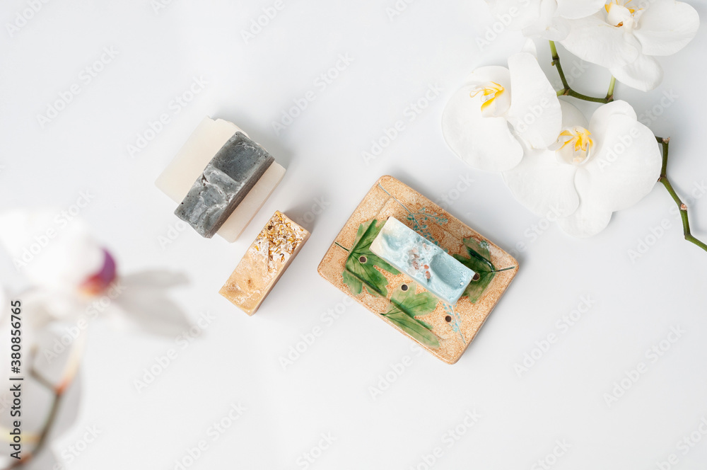 Natural handmade soap bar in ceramic soap dish with orchid flowers on white table