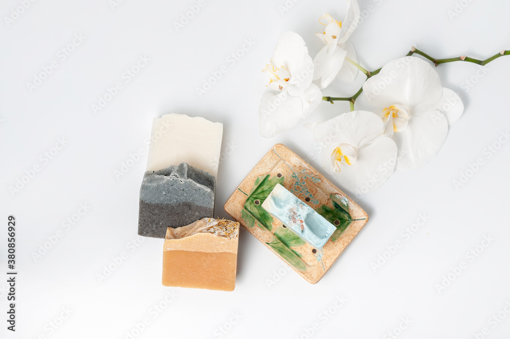Natural handmade soap bar in ceramic soap dish with orchid flowers on white table