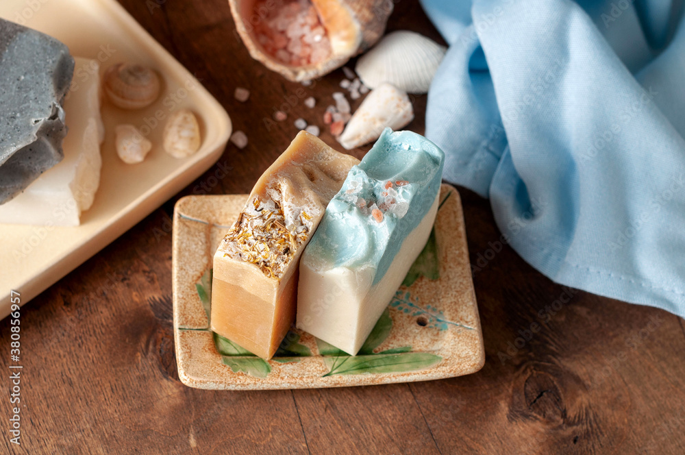 Natural handmade soap bar in ceramic soap dish with spa accessories on wooden table