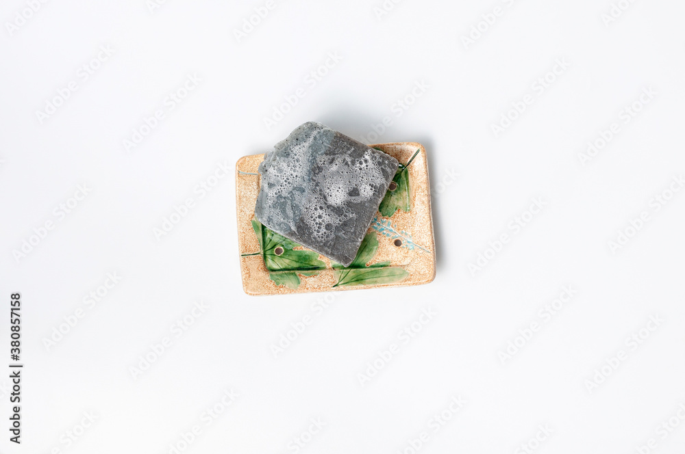 Natural handmade soap bar in ceramic soap dish on white background