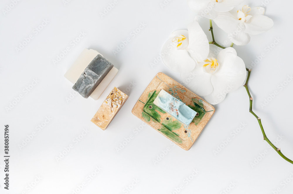 Natural handmade soap bar in ceramic soap dish with orchid flowers on white table