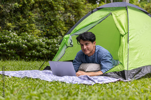 Young man using computer notebook to check news in front of a tent while camping on a holiday