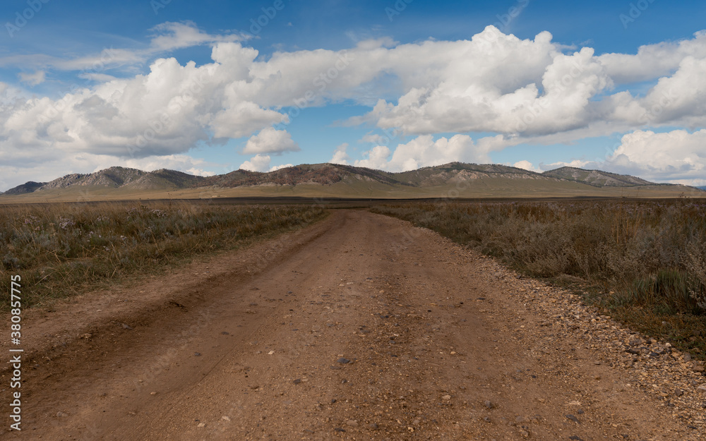 Landscape with a wide dirt road going through the steppe up to the hills. Dirt country road in Khakassia. Landscape with a wide dirt road going through the steppe up to the hills. Dirt country road in Khakassia.