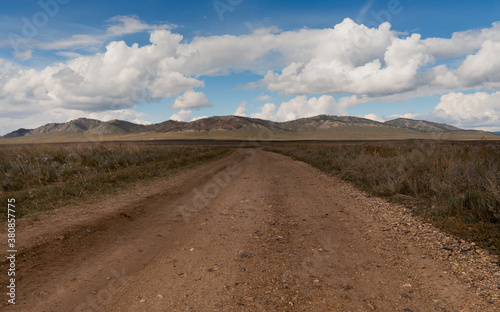 Landscape with a wide dirt road going through the steppe up to the hills. Dirt country road in Khakassia.