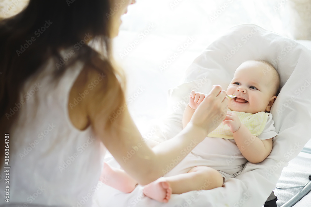 Maternity concept. A young mother feeds her little baby. First lure and breastfeeding. Family in white clothes.