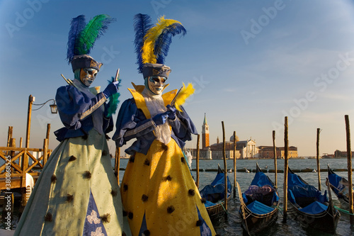 The Carnival of Venice: Molo San Marco, Venice, Italy. Masked revellers pose in front of the Basin of St Mark, with gondolas and the Chiesa di San Giorgio Maggiore in the background