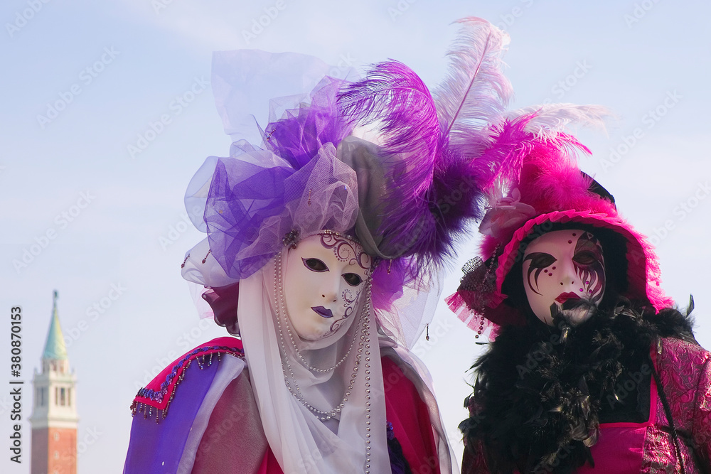 The Carnival of Venice: San Marco, Venice, Italy. Elaborately costumed revellers pose in front of the Basin of St. Mark, with the campanile of the church of San Giorgio Maggiore beyond