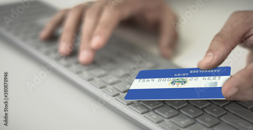 Man pays online with plastic bank card with printed flag of El Salvador. Fictional numbers