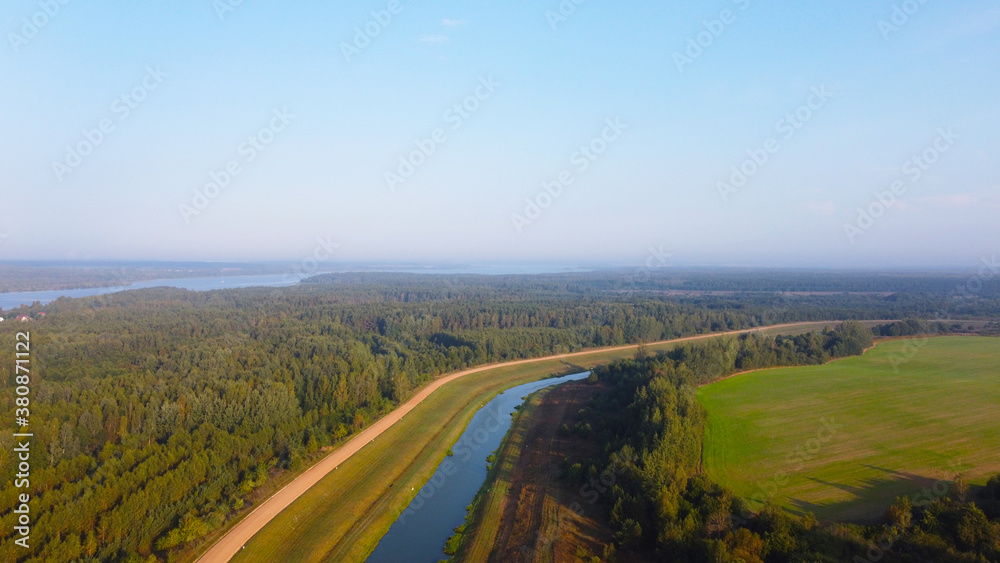 A view from the sky to a blue narrow flat river in the fields