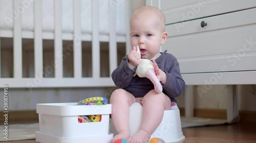 Newborn baby sitting on the potty and playing with toys