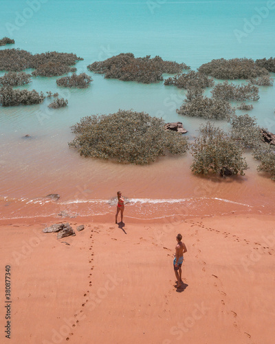 Couple standing on red sand beach and turquoise water
