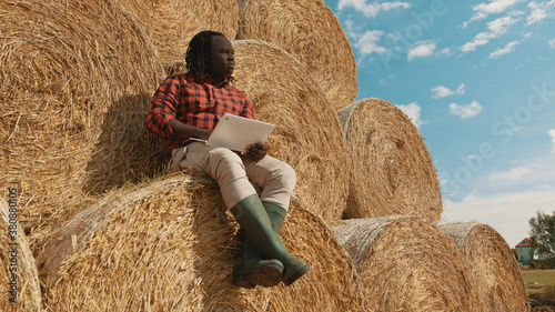 African black farmer sitting on the haystack and working on the laptop. High quality photo