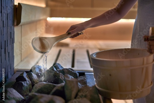 Woman in sauna - real, authentic moment. Women pouring water to hot stones to produce steam.  photo