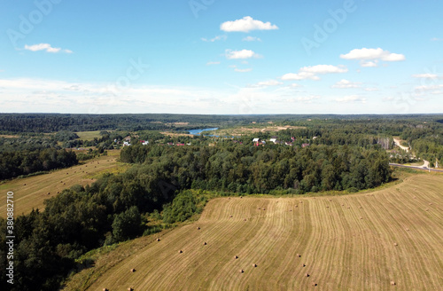 View from drone to the countryside summer fields with many rolled haystacks and forests stretches to the skyline on bright sunny day high view