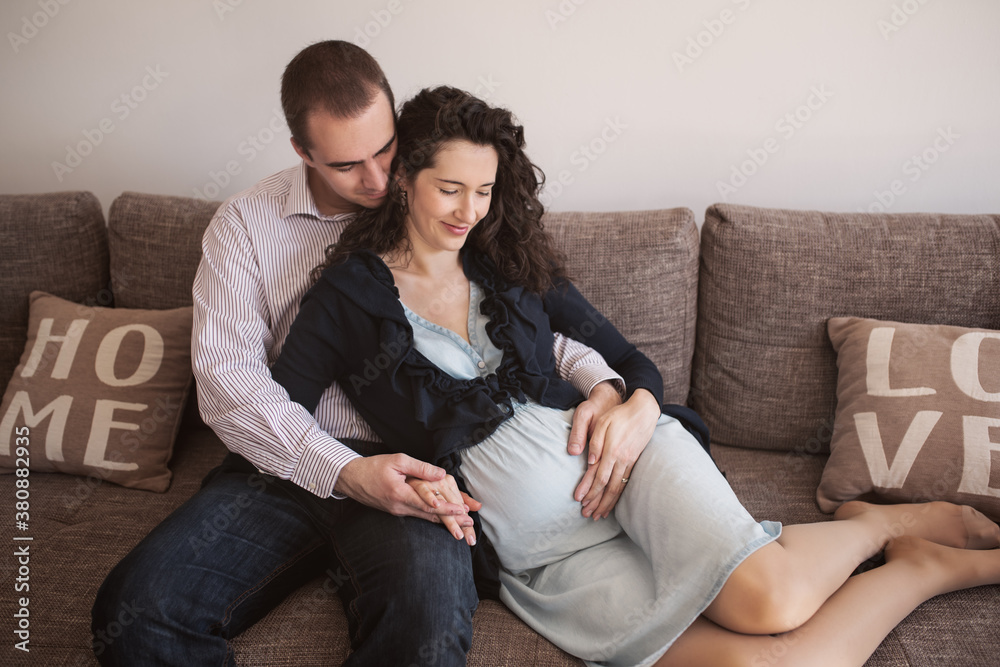 A beautiful pregnant woman snuggling on a sofa with her husband. A beautiful pregnant woman snuggling on a sofa with her husband.