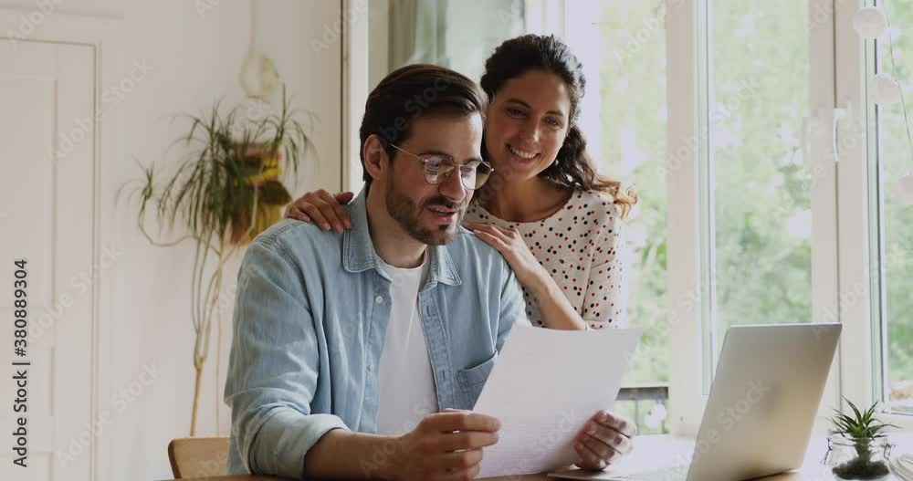 Millennial couple happy wife and husband reading good news in received document letter correspondence feels satisfied enjoy pleasant information. Discuss domestic bills, glad by taxes refund concept