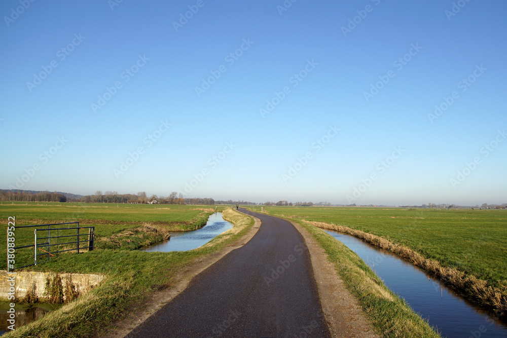 Pasture landscape in North Holland in winter. A narrow road through the meadows with a ditch along the road. Netherlands, December