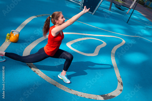 Young female athlete doing workout, training with a kettlebell in the open air.