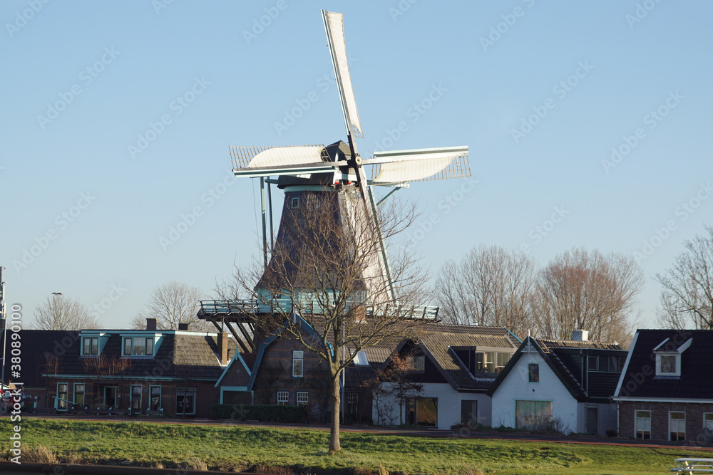 Scaffolding mill, windmill in the Dutch village of Koedijk behind the houses. The blades turn in the wind. It is a flour mill. Netherlands, December 