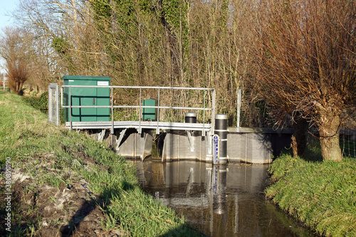 Very small Dutch weir (Dutch: klepstuw) in a ditch. The weir regulates the water drainage capacity of the surface water body. There is a water level meter in the ditch. Netherlands, Bergen. 