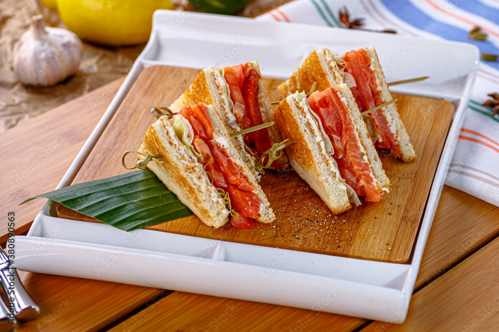 Salmon and tomato sandwiches are on a wooden Board Salmon and tomato sandwiches are on a wooden Board