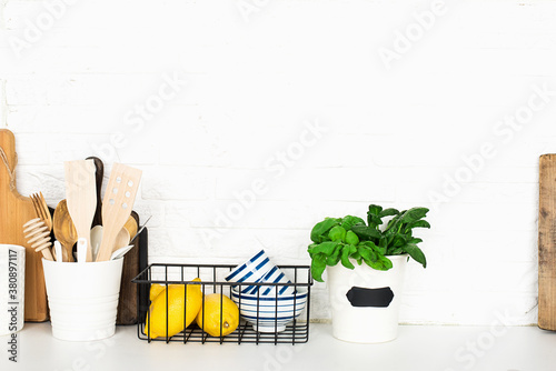 Kitchen table shelf with cutlery, spoons, spatulas, fresh basil, cutting boards, fresh vegetables, lemon on a simple wall. Horizontal, space,