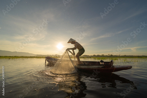 Silhouette Fisherman casting or throwing a net for catching freshwater fish in nature lake or river with reflection in morning time in Asia in Thailand. People.