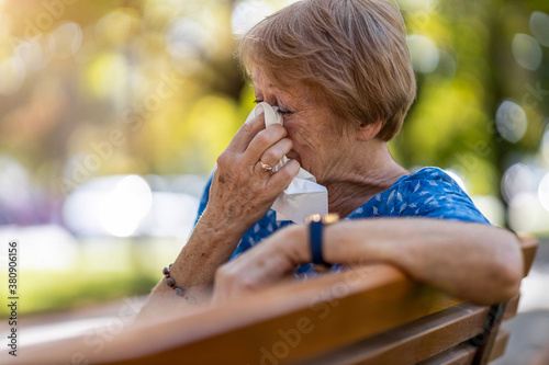 Unhappy senior woman wipes her eyes with a tissue outdoors
