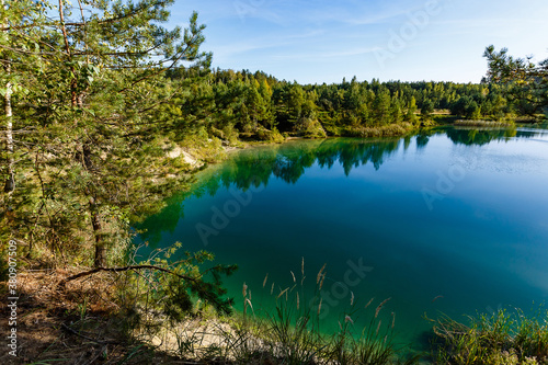 Blue lake in forest on bright sunny day, rural landscape. Trees reflections on water surface. Fresh air concept