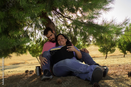 Heterosexual couple reading a book sitting in the forest at the feet of one and they are very happy © Carlos