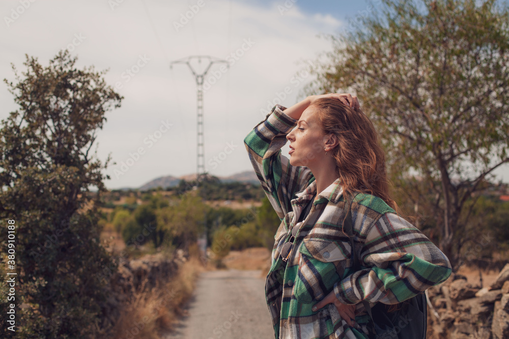 A pretty woman cares her ginger hair while looks off the side of a trail