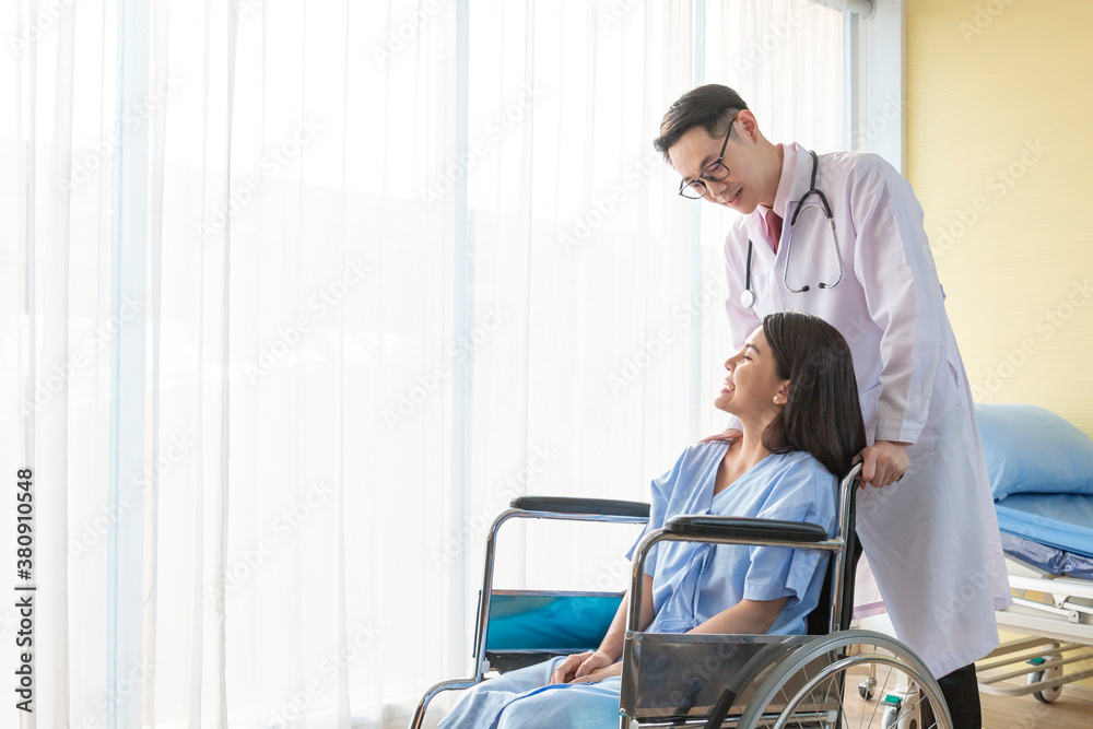 Young Doctor talking to woman in wheelchair after an operation. Smiling doctor looking at a female patient on a wheelchair in hospital. Photo of positive doctor and patient on wheelchair. Young Doctor talking to woman in wheelchair after an operation. Smiling doctor looking at a female patient on a wheelchair in hospital. Photo of positive doctor and patient on wheelchair.