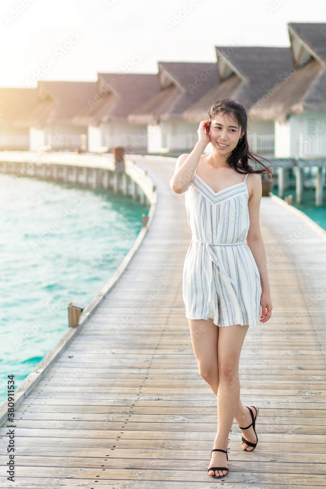 Young girl in a white is walking along a wooden pier. Young pretty woman standing on the wooden beach pier. Young girl in white on a wooden pier on summer sun. Vacation and Travel holiday concept. Young girl in a white is walking along a wooden pier. Young pretty woman standing on the wooden beach pier. Young girl in white on a wooden pier on summer sun. Vacation and Travel holiday concept.