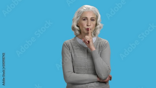 Senior woman showing silence gesture. Portrait of mature lady in gray sweater making silence gesture with forefinger against color background. photo