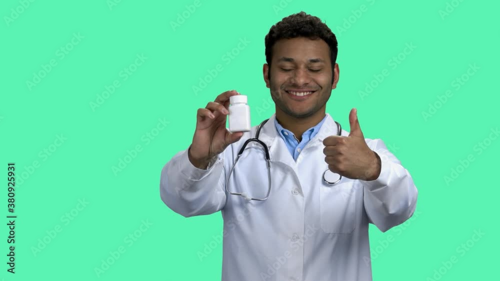 Smiling male doctor showing pills and thumb up. Attractive dark-skinned medical worker looking at camera on turquoise background. Smiling male doctor showing pills and thumb up. Attractive dark-skinned medical worker looking at camera on turquoise background.