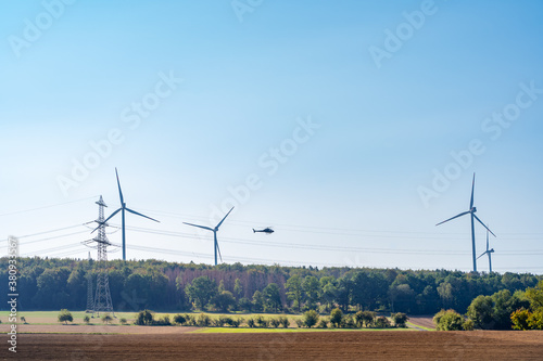 Helicopter flies between wind turbines and overhead power lines