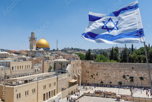 Foto An Israeli flag blows in the wind as jewish orthodox believers read the Torah and pray facing the Western Wall, also known as Wailing Wall or Kotel in Old City in Jerusalem, Israel