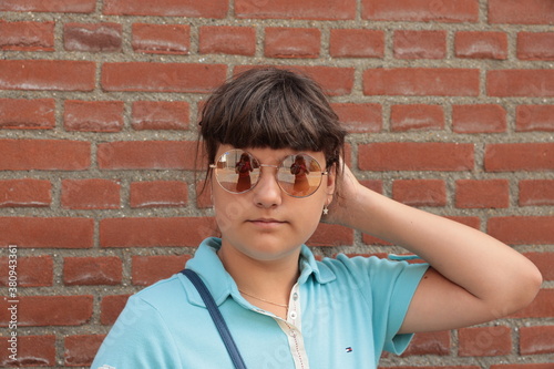 close uo portrait of caucasian young beautiful girl with round glasses, red bricks background outdoor shoot