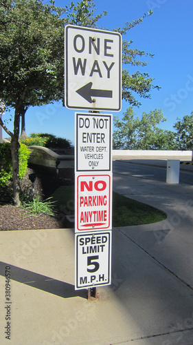 Cuatro letreros que prohíben cosas en la calle, en un solo poste indicador. Solo ida, límite de velocidad, sin estacionamiento, no ingrese.