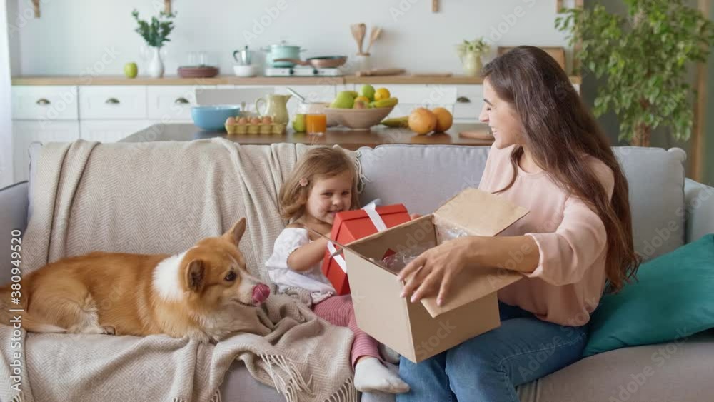 Adorable Girl Unpacking the Order. Happy Mother and Daughter Unpacking the Order. A Young Girl Takes From the Carton Box a Red Present. Mother and Girl Feeling the Pleasant Surprise. Adorable Girl Unpacking the Order. Happy Mother and Daughter Unpacking the Order. A Young Girl Takes From the Carton Box a Red Present. Mother and Girl Feeling the Pleasant Surprise.